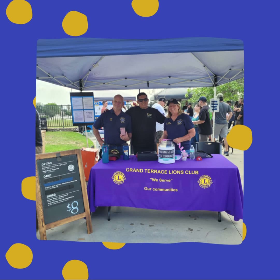 Three Grand Terrace Lions members behind a purple club-branded table at the Blue Mountain Festival, with a donations jar on the table.